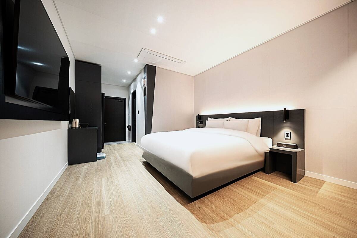 Een moderne hotelkamer met een groot bed, een nachtkastje, een ingebouwde televisie en een houten vloer.