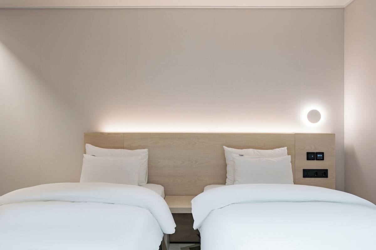 Een hotelkamer met twee bedden, een houten hoofdbord en een wandlamp.
