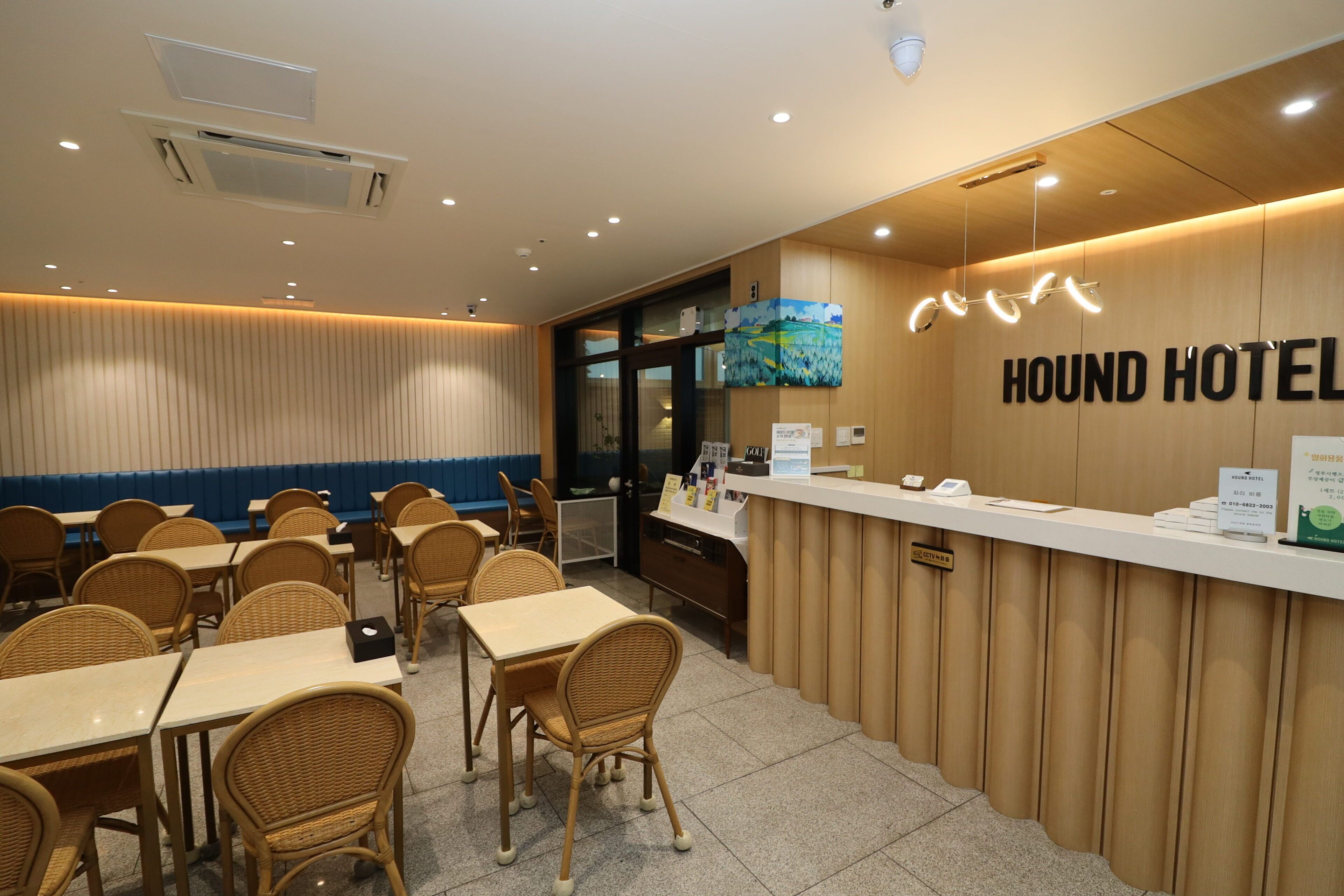 A hotel reception area with a wooden counter, a sign reading "HOUND HOTEL," and several tables and chairs arranged for guests.