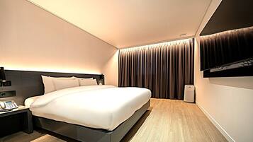 Habitació d'hotel moderna amb un llit gran, una taula de nit amb telèfon i una televisió penjada a la paret.