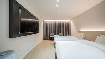 Una habitación de hotel moderna con una televisión de pantalla plana grande montada en la pared, una cama, una mesita de noche, una silla y una ventana con cortinas.