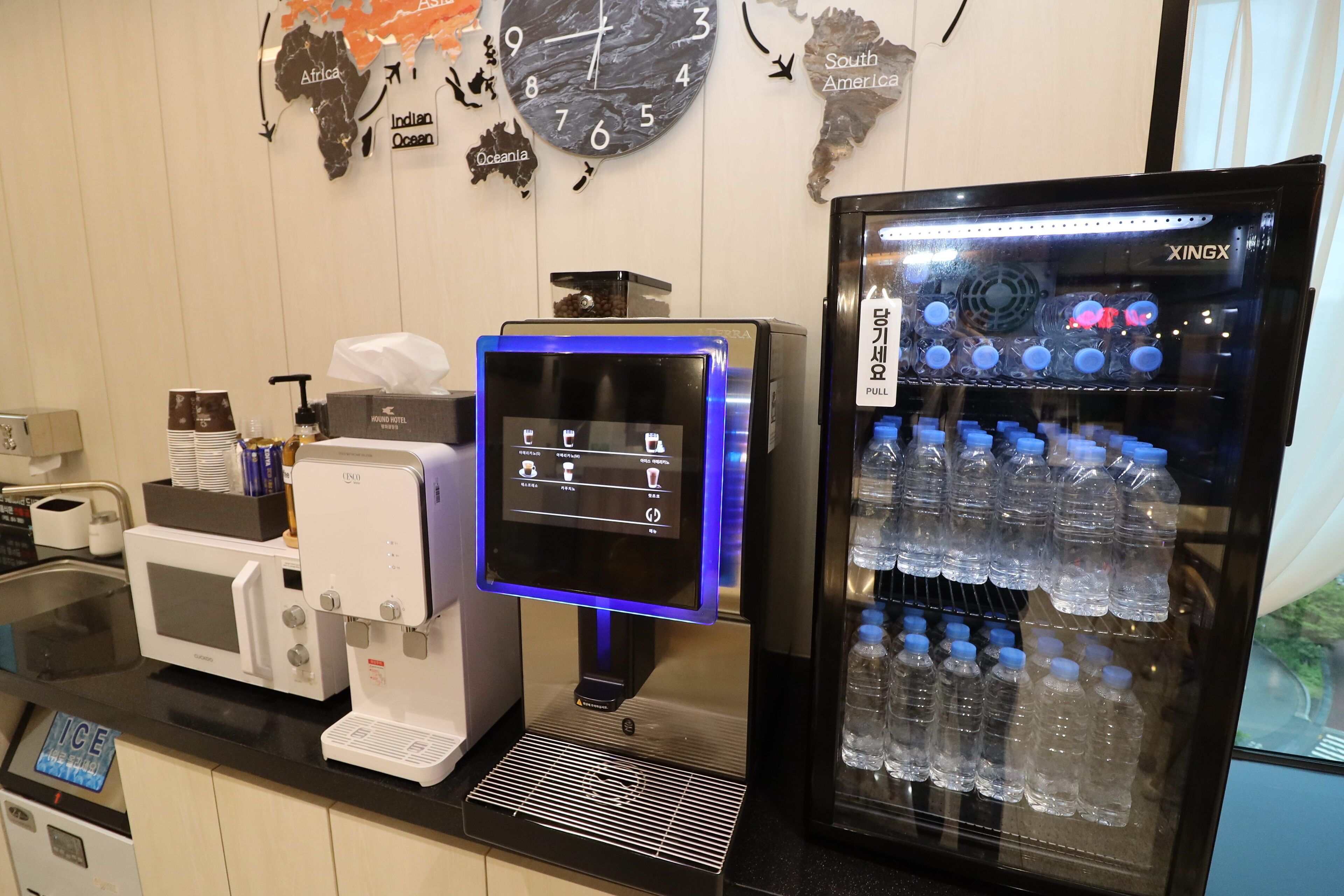 A hotel reception area with a coffee machine, a digital display, and a water dispenser.