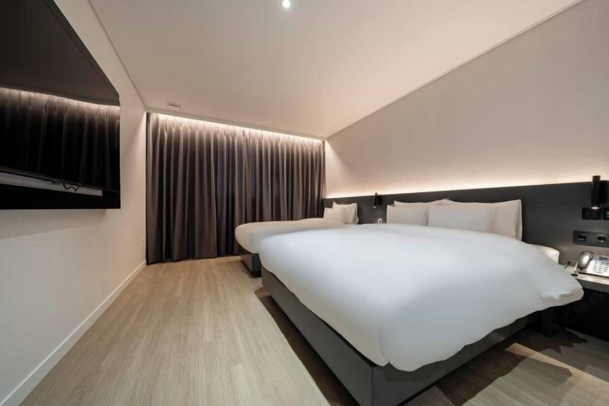 Een moderne hotelkamer met een groot bed, een nachtkastje met een telefoon en een aan de muur bevestigde televisie.