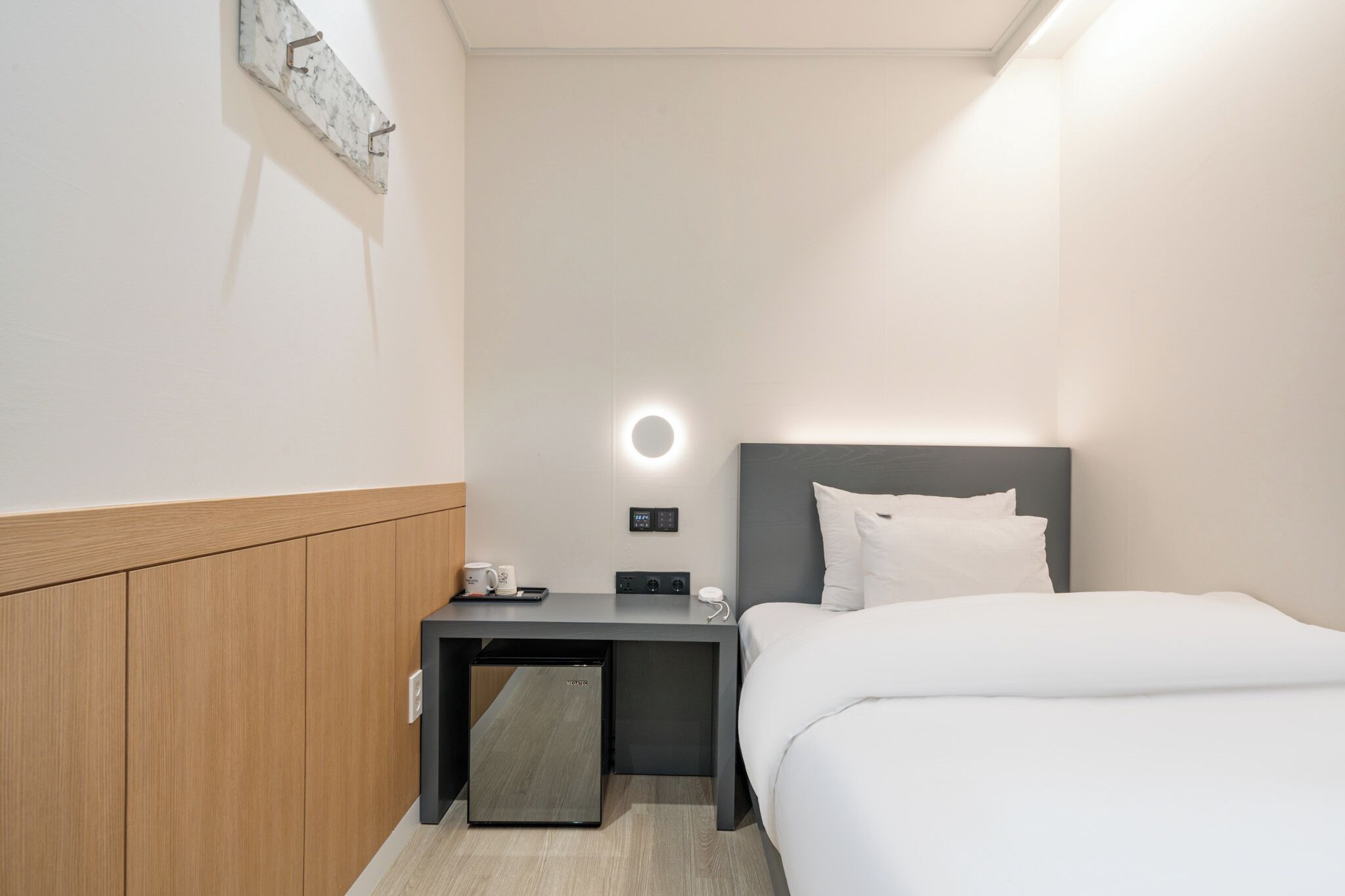 Une chambre d’hôtel avec un lit, une table de chevet et un petit bureau avec une lampe.