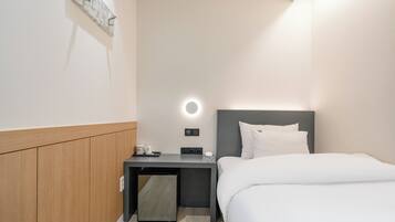Une chambre d’hôtel avec un lit, une table de chevet et un petit bureau avec une lampe.