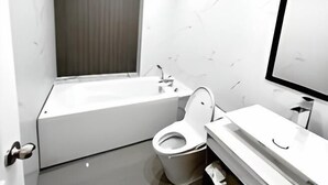 A modern bathroom with a bathtub, toilet, and a large mirror. - Rose Hotel - by Bay Luxury (Ho Chi Minh City)