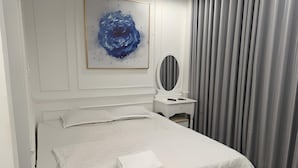A neatly made bed with white linens, a bedside table with a mirror, and a painting on the wall. - Rose Hotel - by Bay Luxury (Ho Chi Minh City)