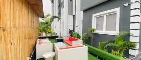 Un pequeño patio exterior con césped artificial, muebles de mimbre blanco y plantas en macetas.