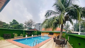 A swimming pool with a wooden deck and chairs, surrounded by greenery and a palm tree. - Presken Hotel Ikoyi (Lagos)