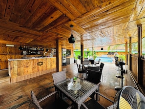 A wooden interior with a bar area, outdoor seating, and a view of a swimming pool. - Presken Hotel Ikoyi (Lagos)
