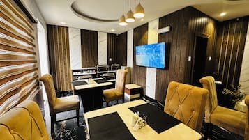 A modern dining area with a marble floor, leather chairs, a central table, and a television mounted on the wall.