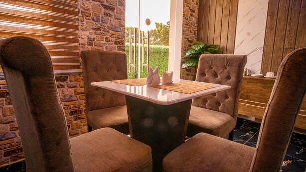 A cozy dining area with a table and four cushioned chairs, set against a stone wall and wooden paneling. - Presken Hotel Ikoyi (Lagos)