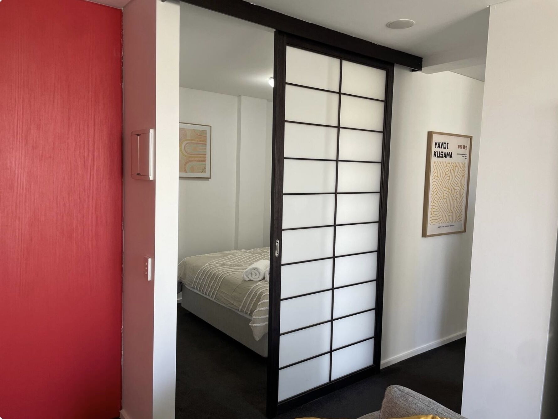 Una habitación con una puerta corrediza de fusuma, una cama con colcha a rayas y un cartel en la pared.