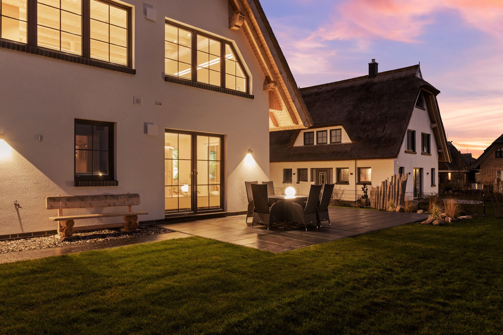 Une maison à deux étages dotée d’un grand patio, d’un coin repas avec des chaises et d’un banc.