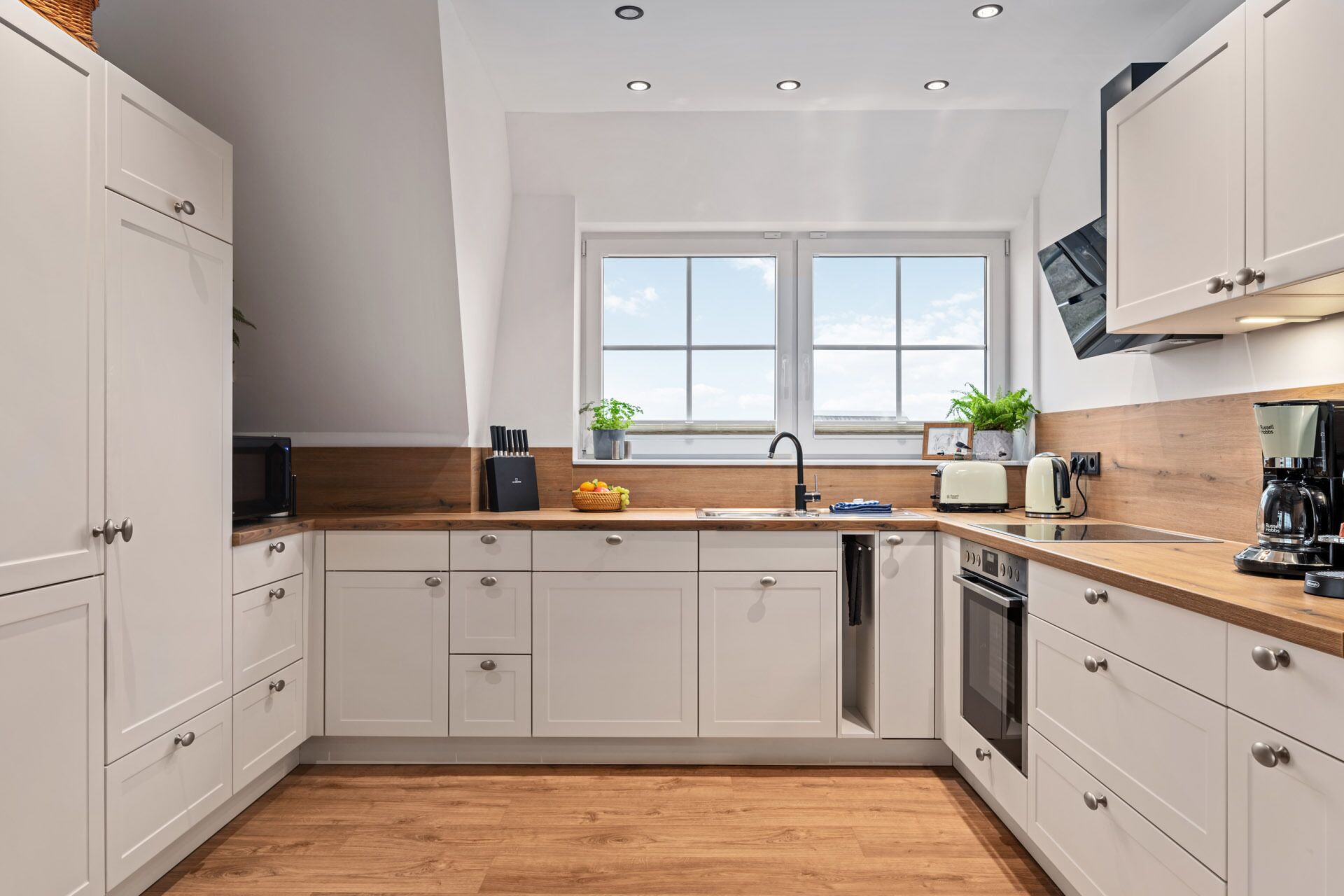 A modern kitchen with white cabinets, a wooden countertop, a built-in oven, and a window above the sink.
