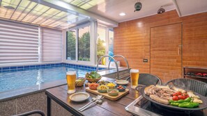 A poolside dining area with a grill, table with plates, bowls of food, and glasses of beer. - Gyeongju Gaeulgapulbilla (Gyeongju)