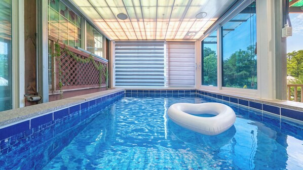 A swimming pool with a floating ring, surrounded by glass walls and a view of greenery. - Gyeongju Gaeulgapulbilla (Gyeongju)