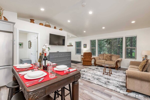 A modern living room with a sofa, armchair, and a dining table set for four.