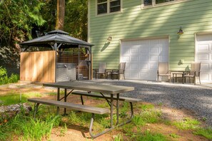 A picnic table with a wooden structure and chairs in front of a house with a garage.