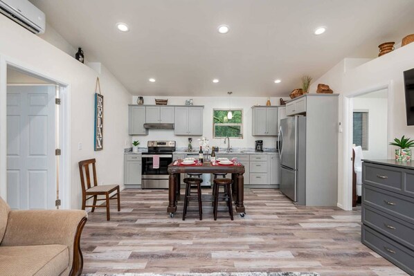 A modern kitchen with grey cabinets, a central island with stools, a refrigerator, and a dining table set for four. - New Listing! Beautiful new construction Sutton lake area home, hot tub, sister home also available (Florence)