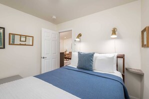 A bedroom with a bed, a white door, two wall-mounted lamps, and a mirror.