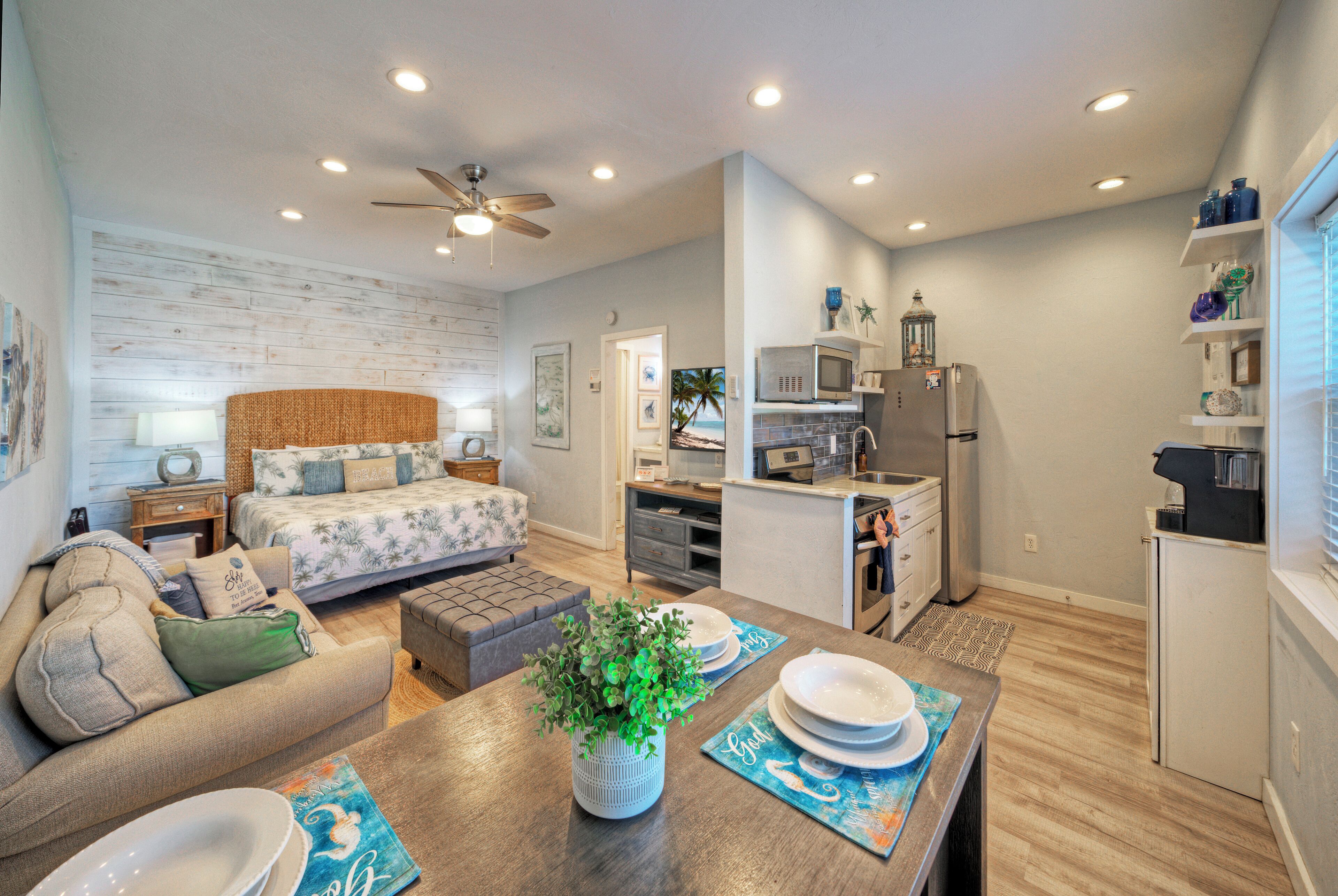 A compact living space with a kitchenette, a dining area with a table and chairs, a sofa, and a ceiling fan.