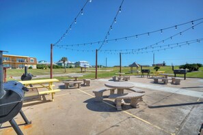 An outdoor patio with picnic tables and a barbecue grill. - Family Studio • Beach Boardwalk + Shared Pools | Golf Cart Zone | Beach Bungalow (Port Aransas)
