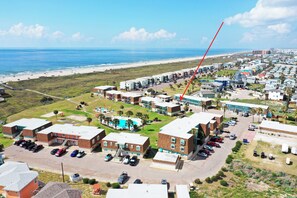 An aerial view of a coastal residential area with a beach, multiple buildings, and a parking lot. - Family Studio • Beach Boardwalk + Shared Pools | Golf Cart Zone | Beach Bungalow (Port Aransas)