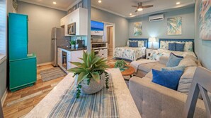 A compact living space with a kitchenette, a dining area, and a bedroom with a bed and two nightstands. - Family Studio • Beach Boardwalk + Shared Pools | Golf Cart Zone | Beach Bungalow (Port Aransas)