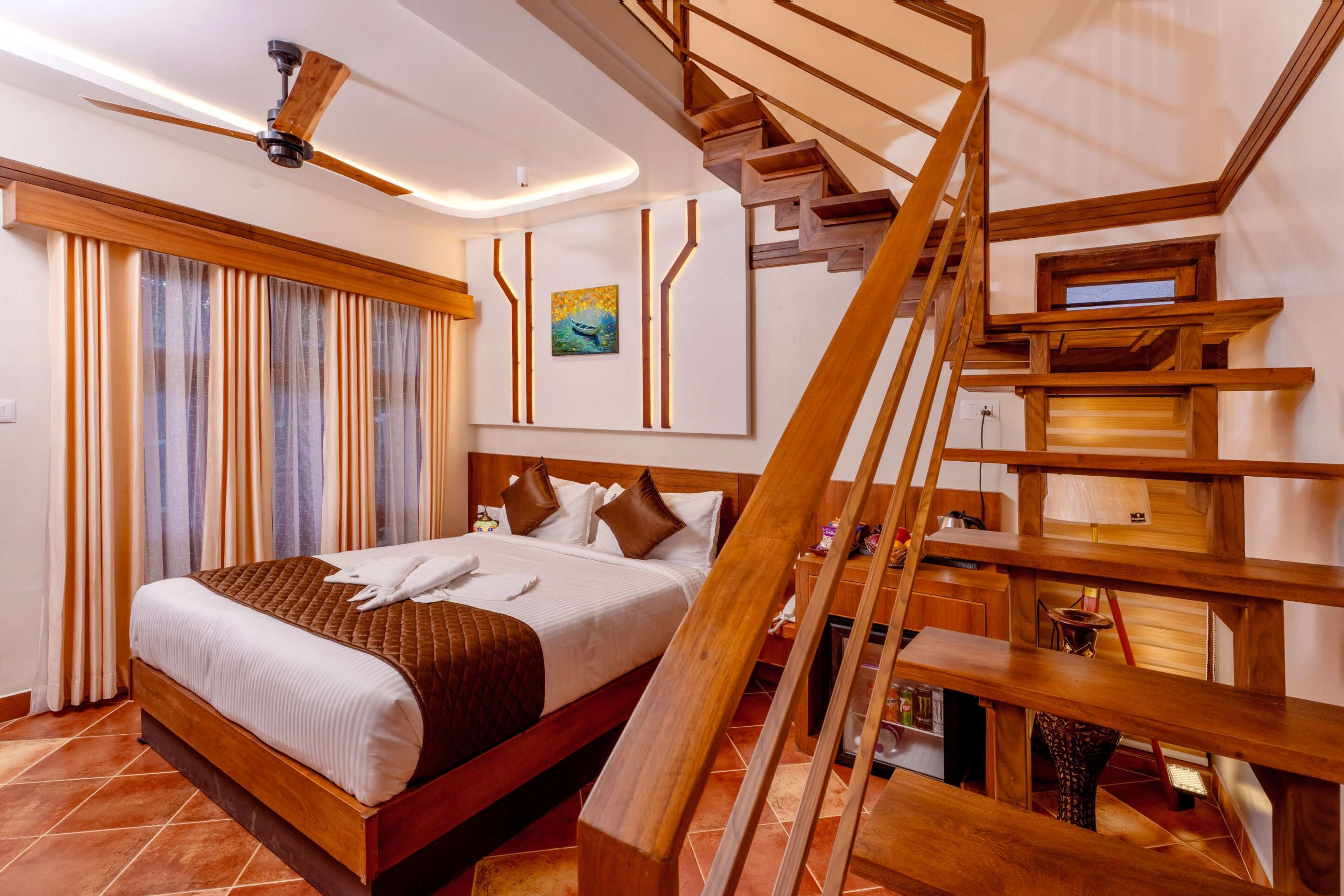 A modern hotel room with a large bed, wooden staircase, and a ceiling fan.