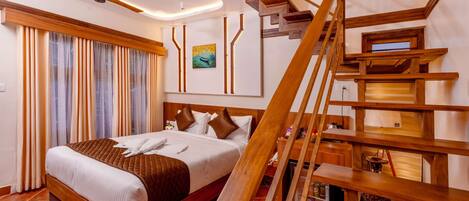 A modern hotel room with a large bed, wooden staircase, and a ceiling fan.
