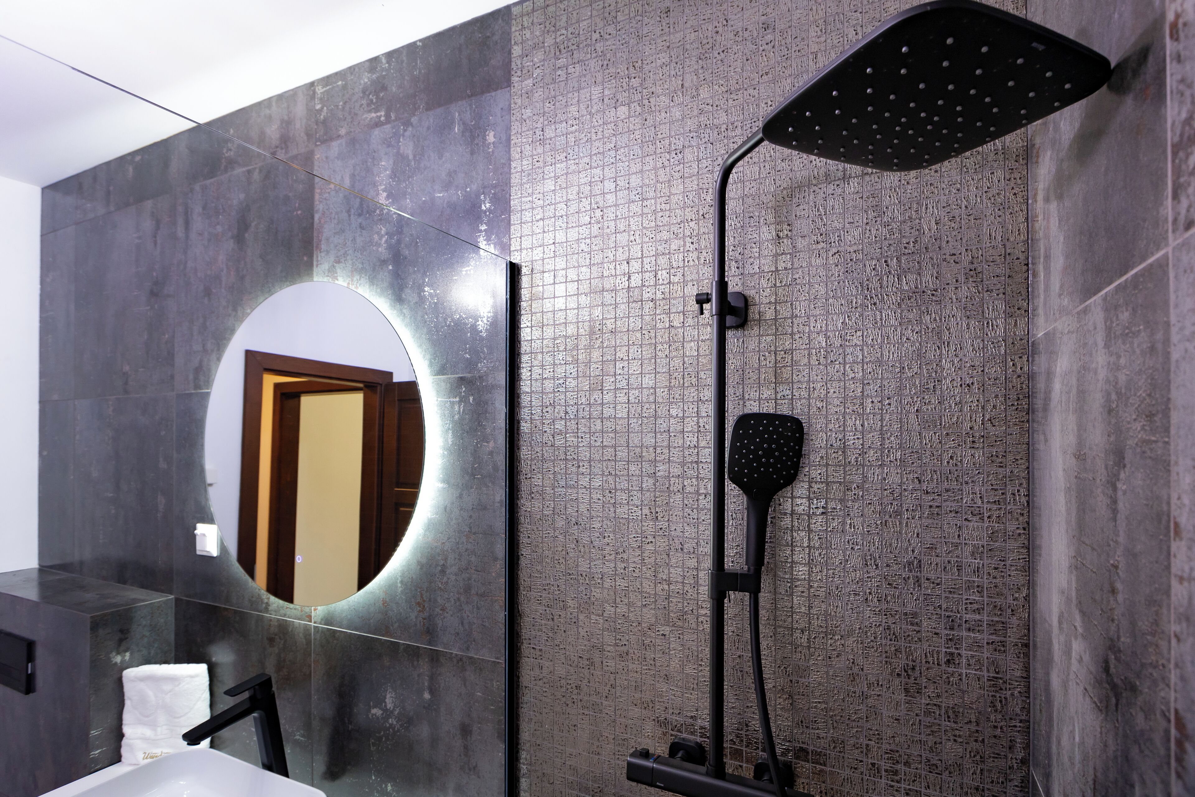 A modern bathroom with a large mirror, a black showerhead, and a white sink.