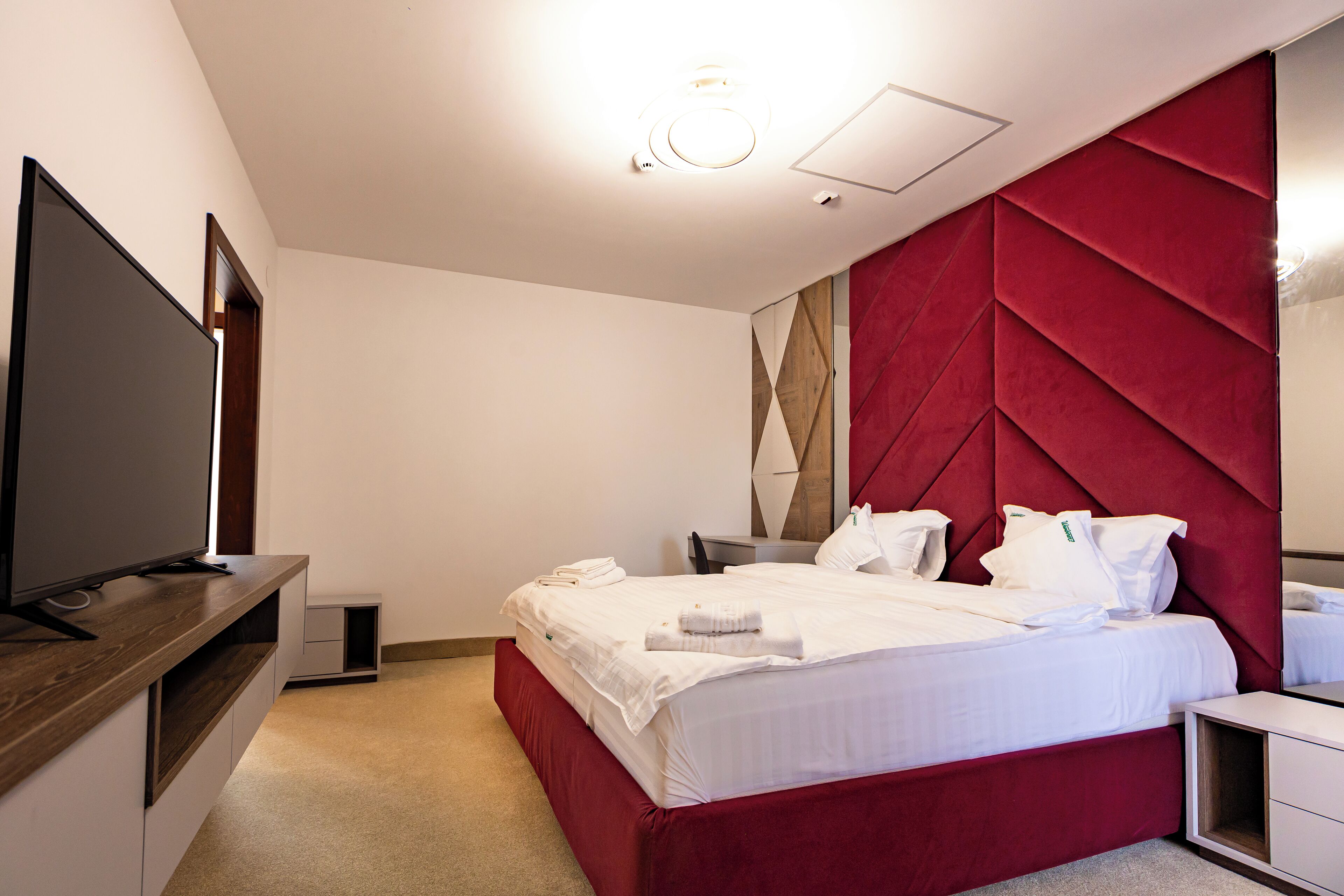 A modern hotel room with a large bed, a flat-screen TV, and a red accent wall.
