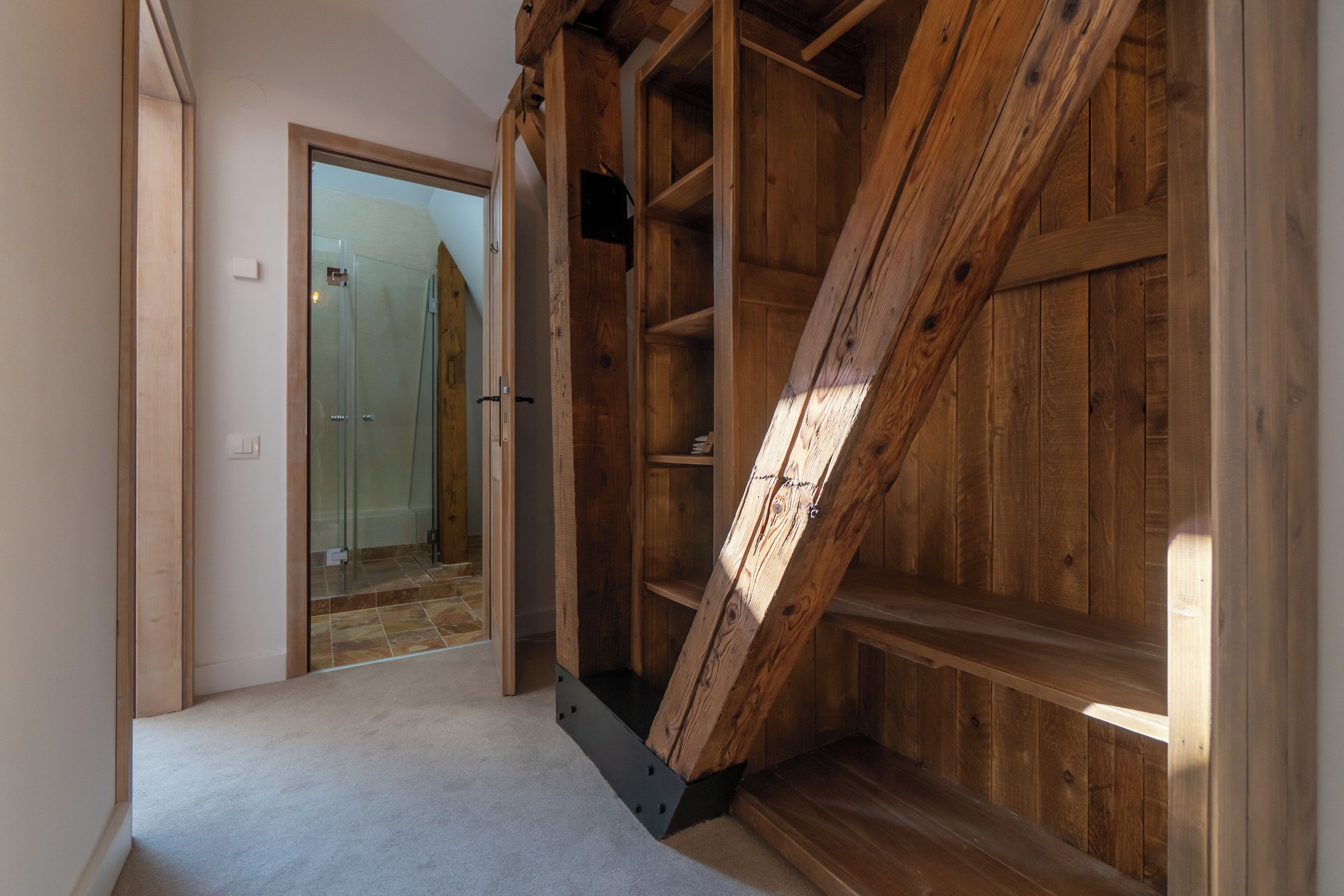 A room with a wooden staircase, a glass door leading to a bathroom, and a carpeted floor.