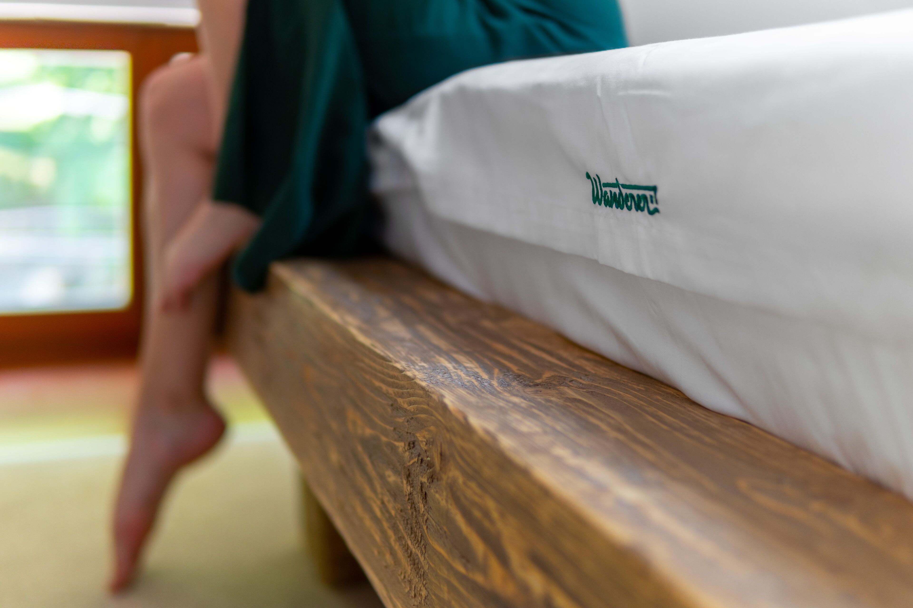 A wooden bench with a white mattress and green pillow.