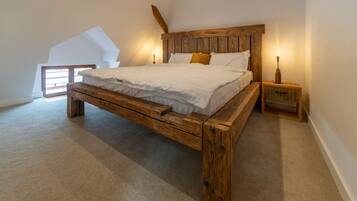 Quarto com estrutura de cama de madeira, roupa de cama branca e duas mesas de cabeceira com abajures.