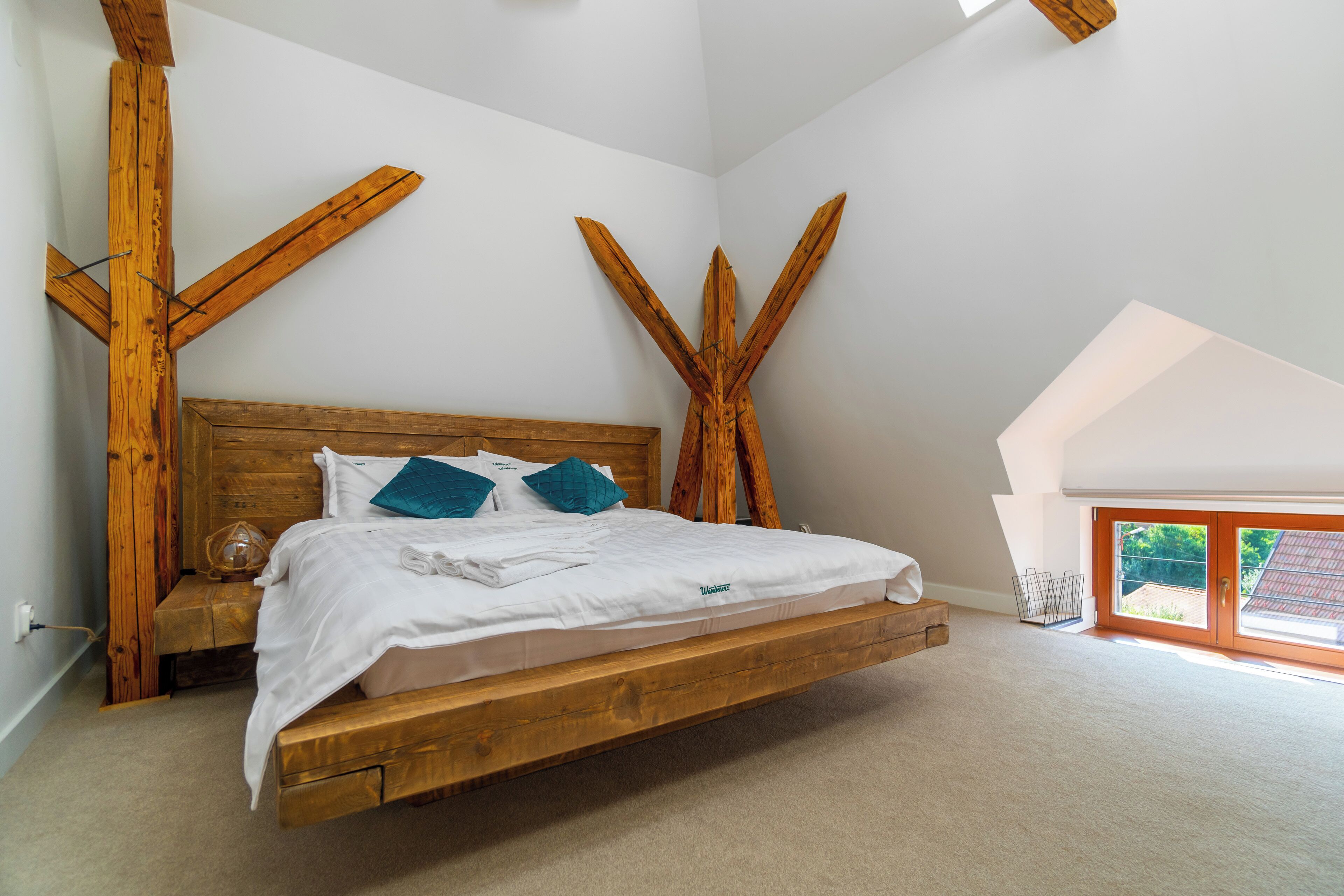 Una camera da letto con un letto in legno, biancheria da letto bianca e un soffitto spiovente.