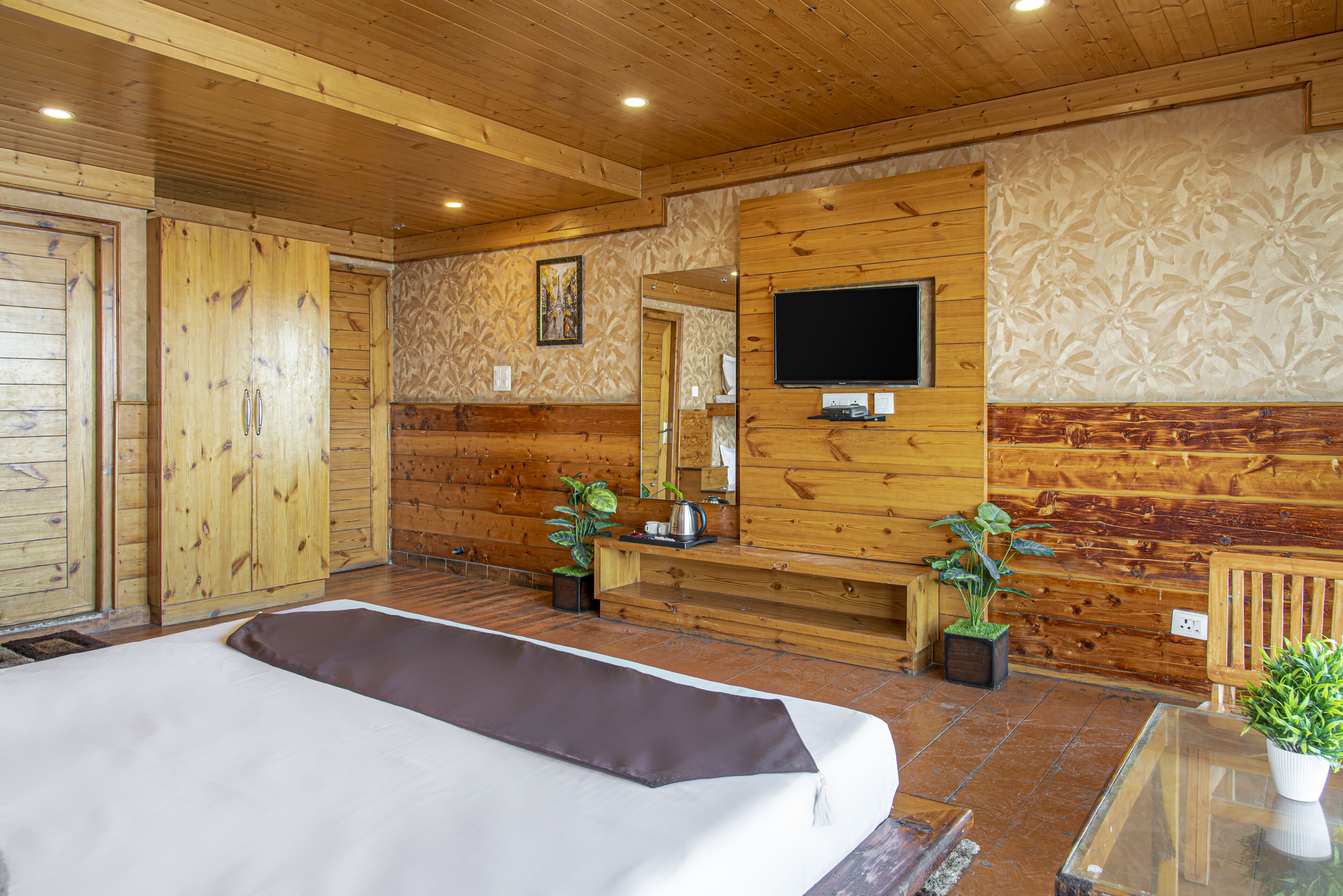 Een kamer in chaletstijl met een bed, een aan de muur bevestigde televisie en twee potplanten.