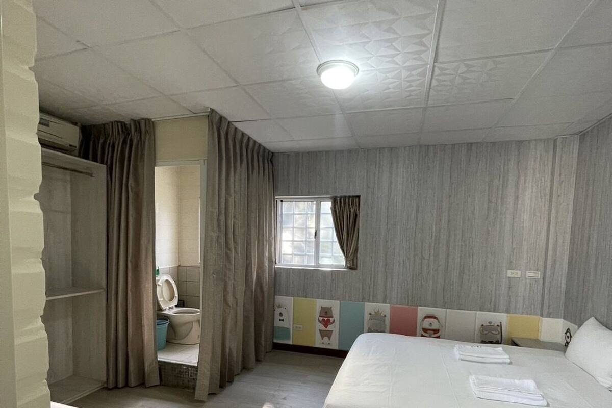 A room with two beds, a window with curtains, a toilet, and a shower area.