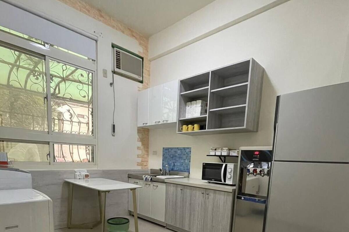 A modern kitchen with white cabinets, a built-in microwave, a refrigerator, and a window with decorative iron bars.