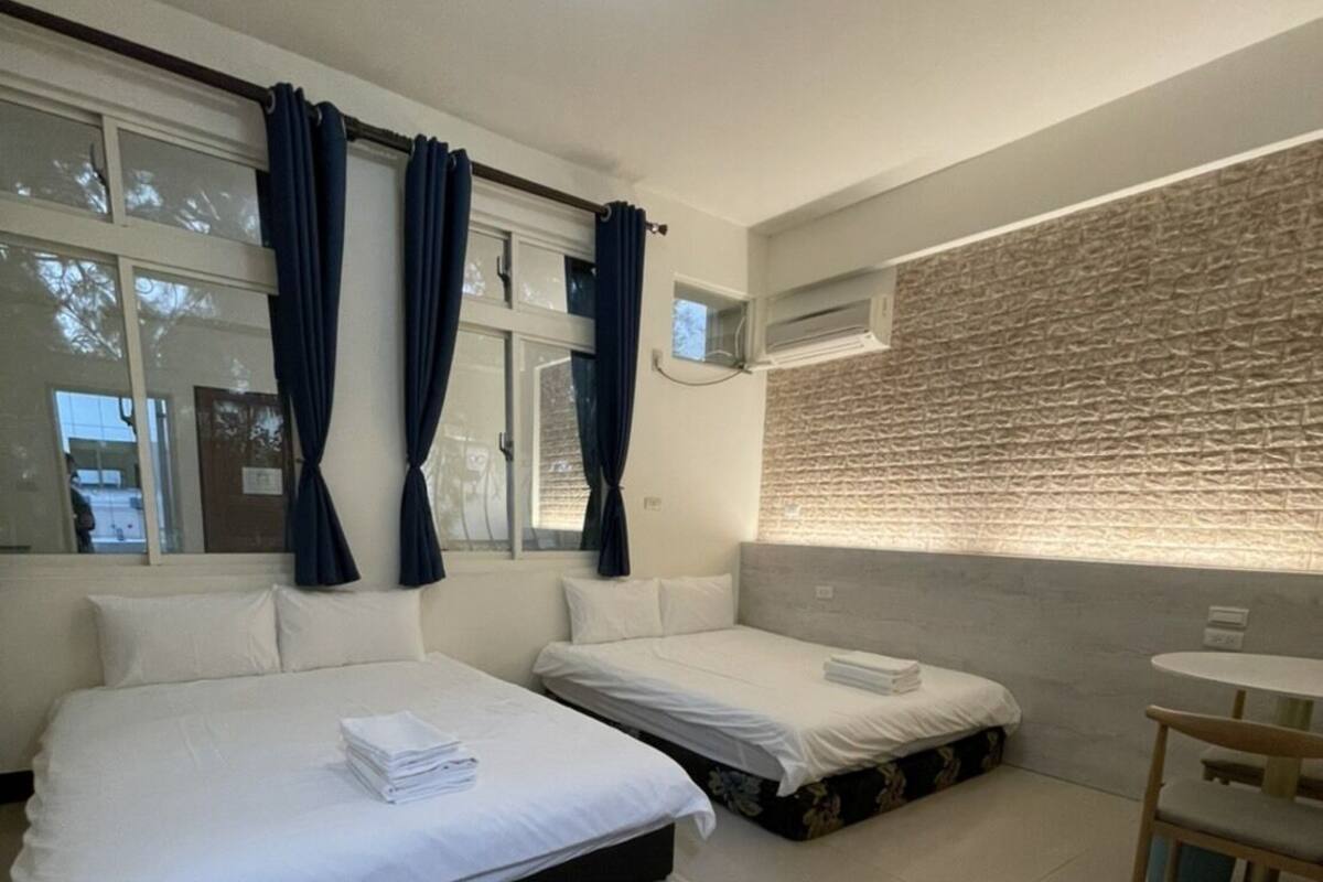 A modern hotel room with two beds, a small table, and a window with curtains.