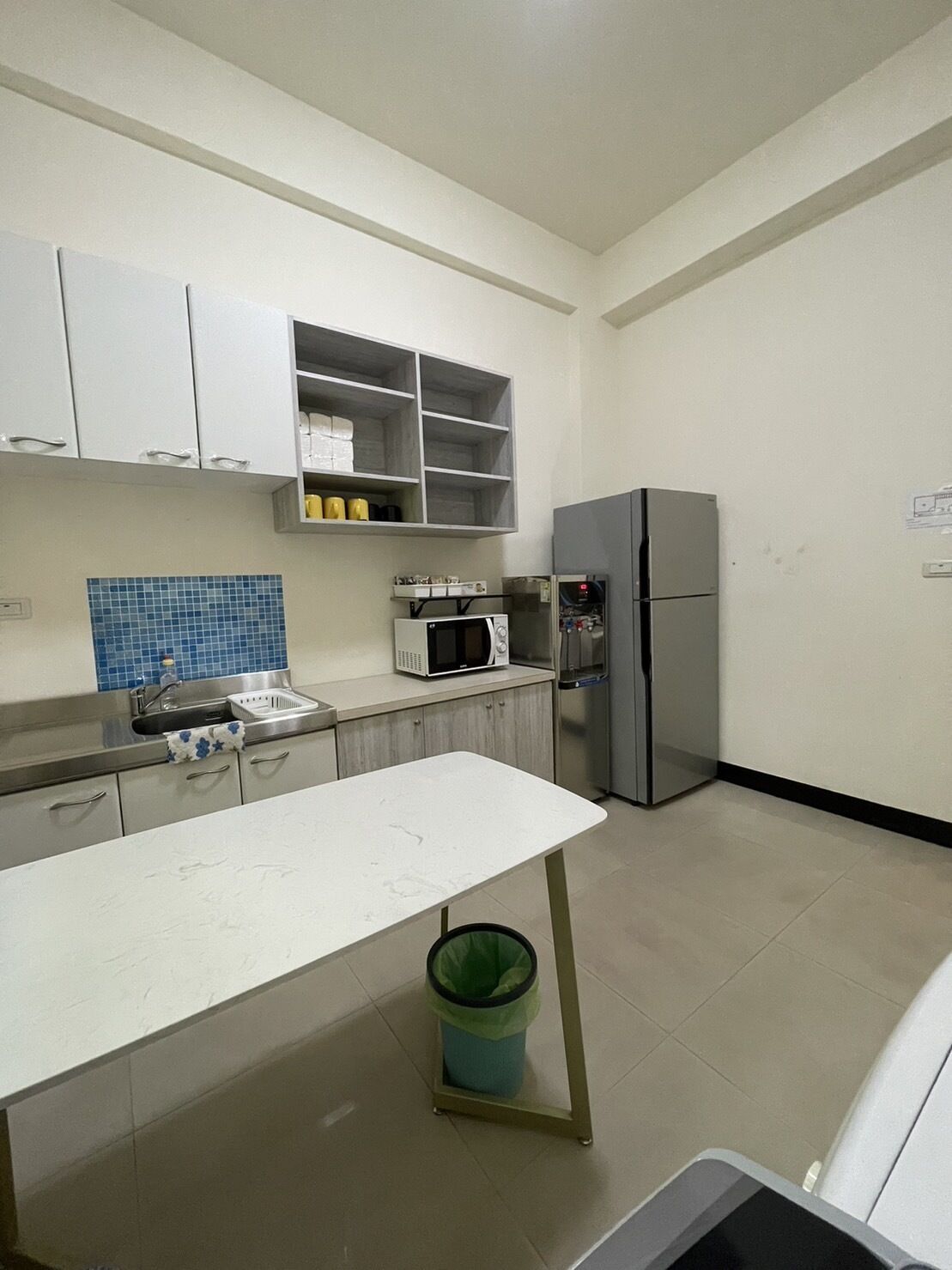 A kitchen with white cabinets, a microwave, a refrigerator, and a trash bin.