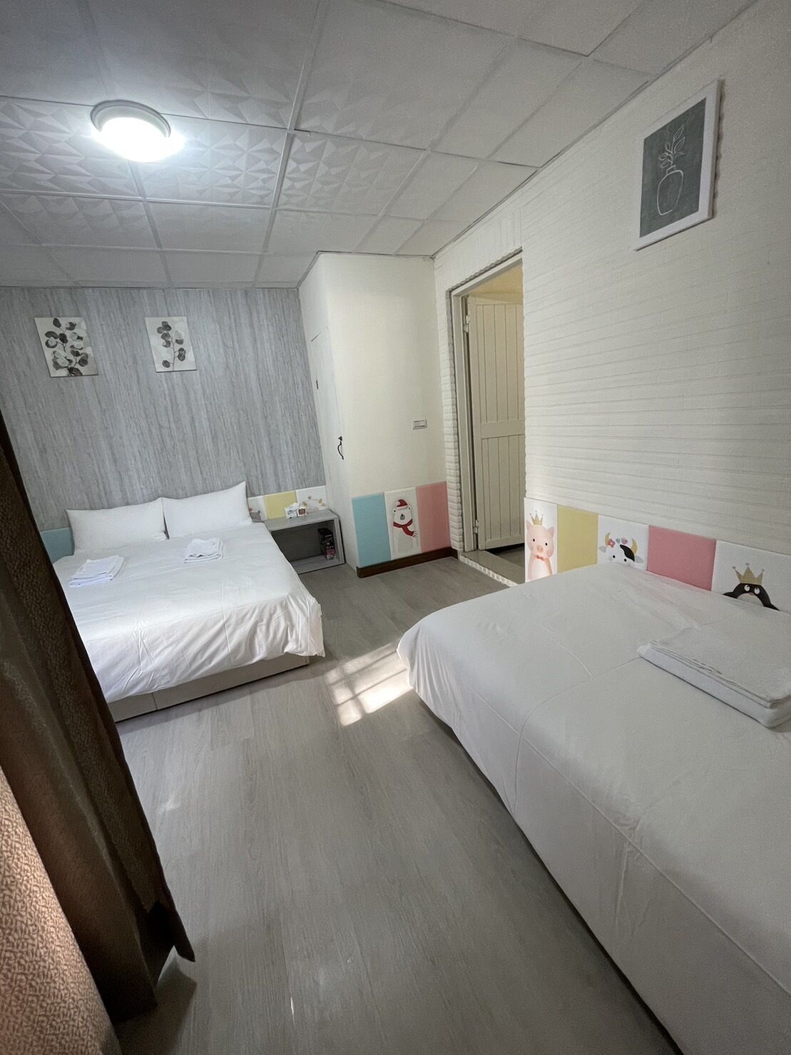A hotel room with two beds, a small bedside table, a nightstand, and a door leading to another room.