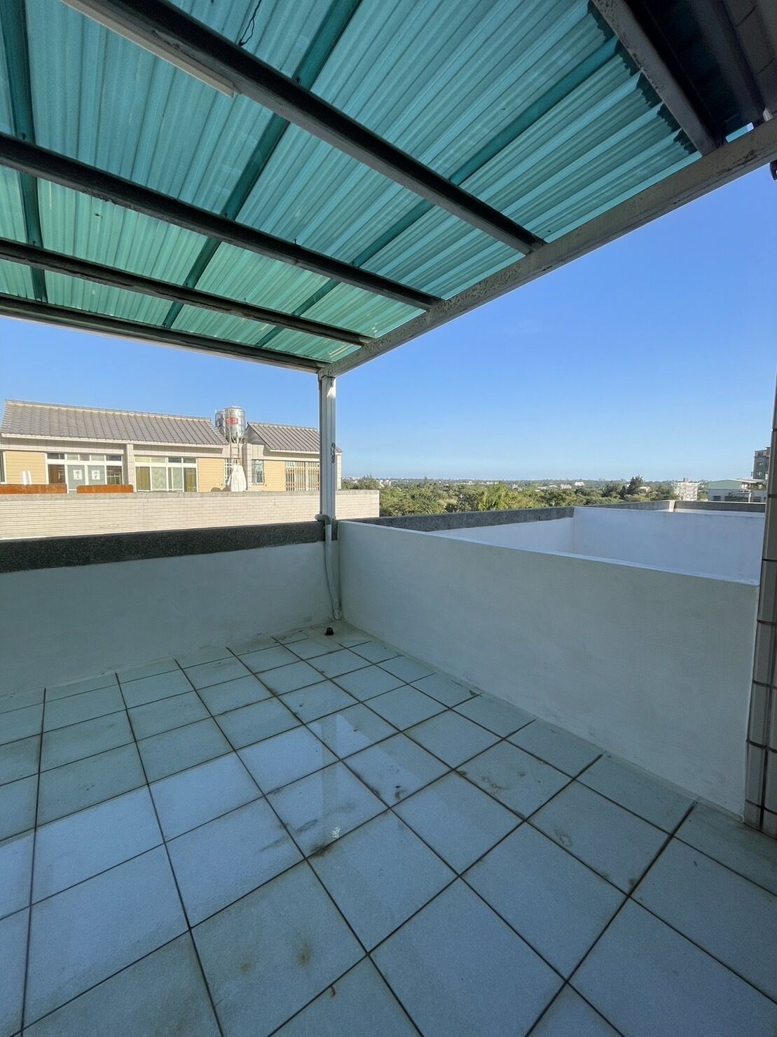 A covered balcony with tiled flooring and a view of a building in the background.