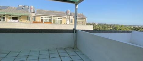A covered balcony with tiled flooring, a metal roof, and a view of buildings in the background.