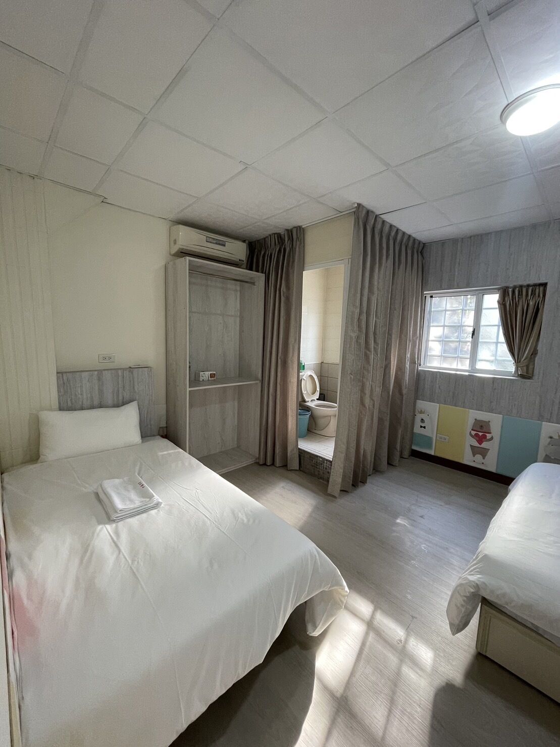 A hotel room with two beds, a bathroom, and a wardrobe.