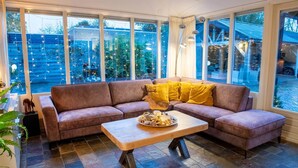 Una sala de estar acogedora con un sofá modular, una mesa de centro de madera y ventanas amplias que ofrecen vistas al exterior.