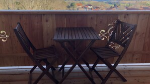 En træterrasse med et bord og to stole, der kigger ud over et naturskønt sølandskab og fjerne bygninger.