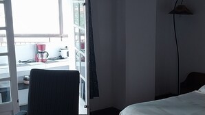 A room with a bed, a chair, a lamp, and a view of the outside. -  Grace Guesthouse (Antananarivo)