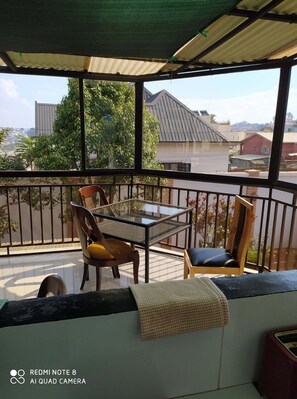 A balcony with a table and chairs, a view of buildings, and a green awning.